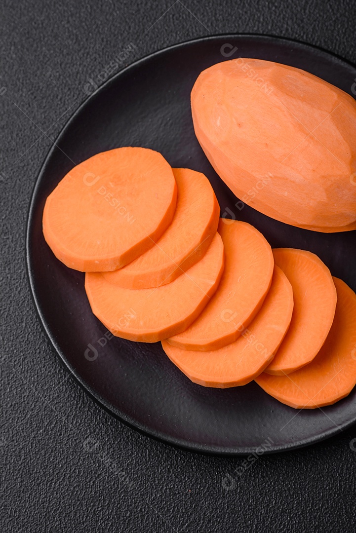 Grandes tubérculos frescos de batata-doce rosa com tomates e especiarias em um fundo escuro. Cozinhando uma refeição vegetariana saudável