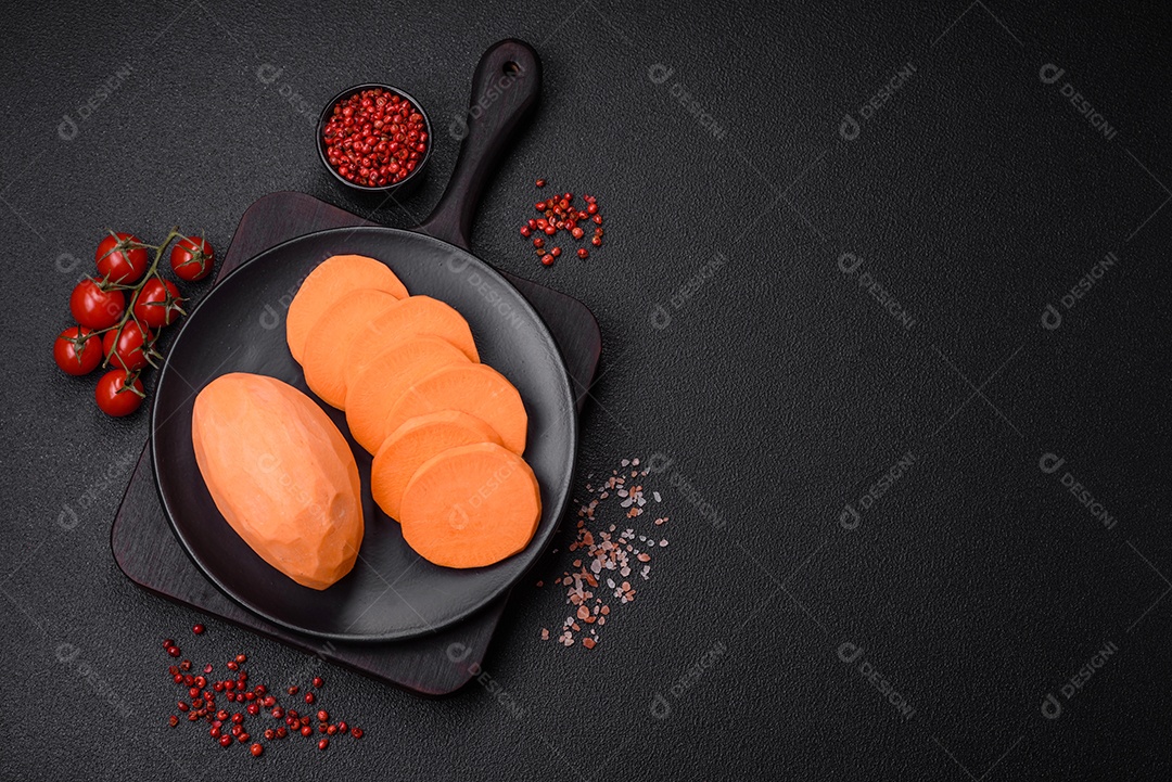 Grandes tubérculos frescos de batata-doce rosa com tomates e especiarias em um fundo escuro. Cozinhando uma refeição vegetariana saudável