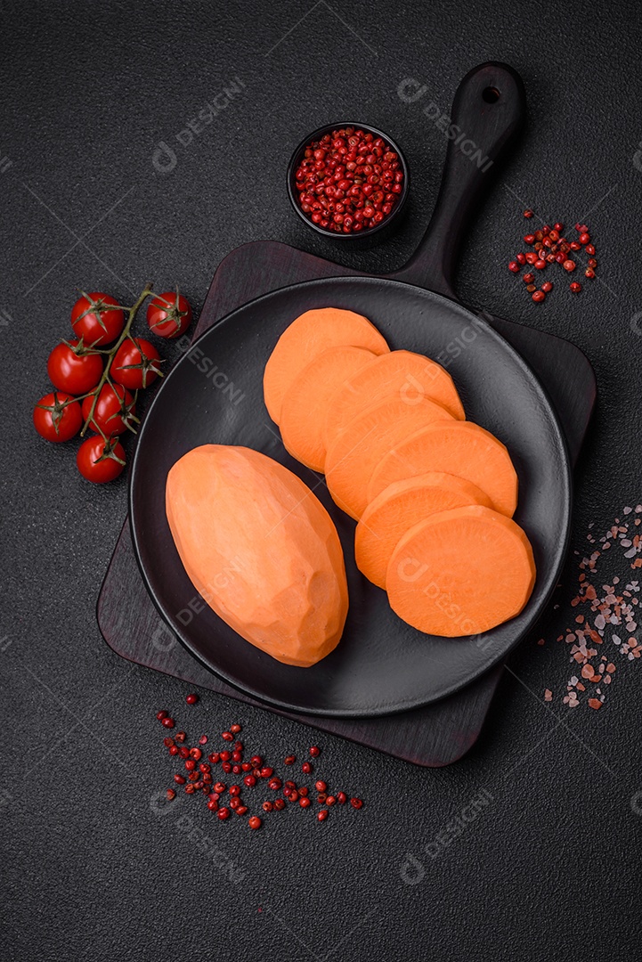 Grandes tubérculos frescos de batata-doce rosa com tomates e especiarias em um fundo escuro. Cozinhando uma refeição vegetariana saudável