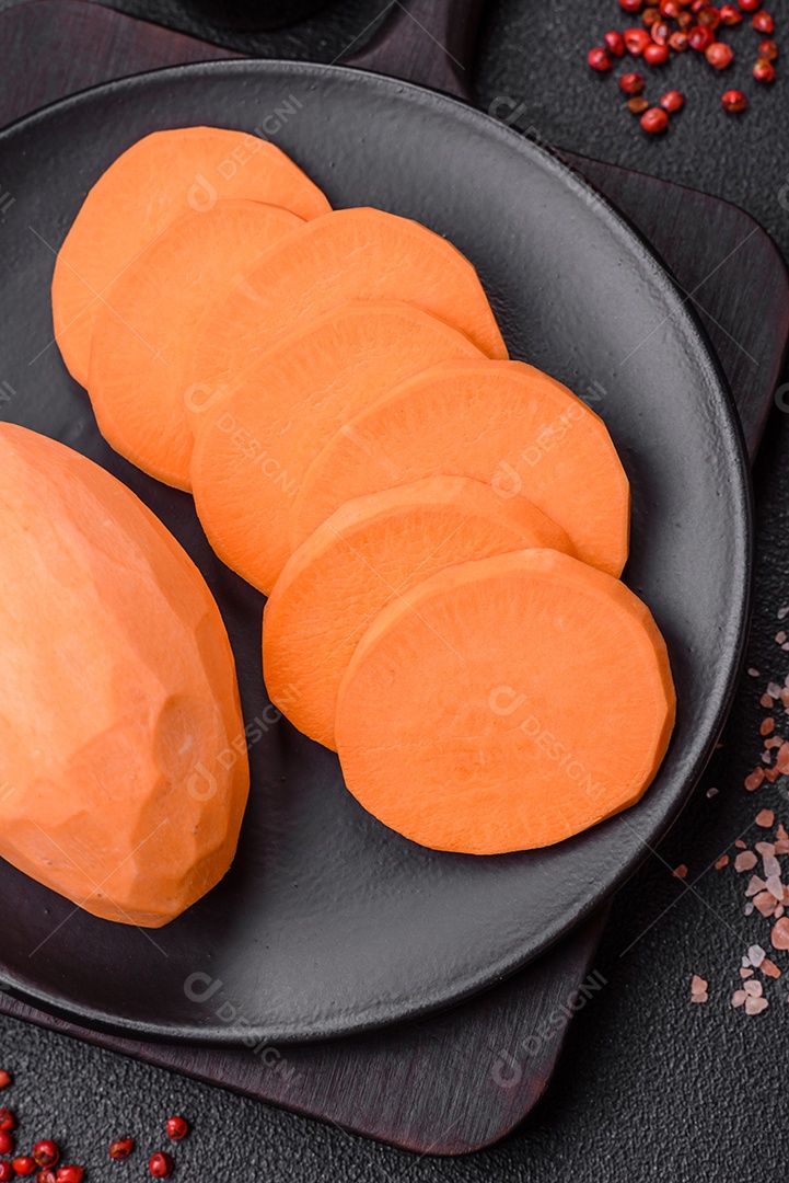 Grandes tubérculos frescos de batata-doce rosa com tomates e especiarias em um fundo escuro. Cozinhando uma refeição vegetariana saudável