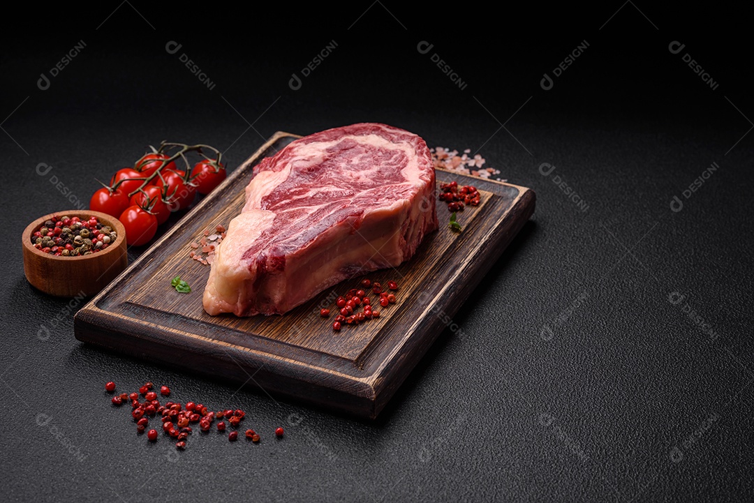Bife fresco e suculento de carne crua com sal e especiarias sobre um fundo escuro de concreto