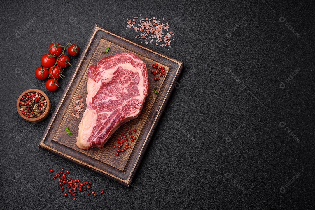 Bife fresco e suculento de carne crua com sal e especiarias sobre um fundo escuro de concreto