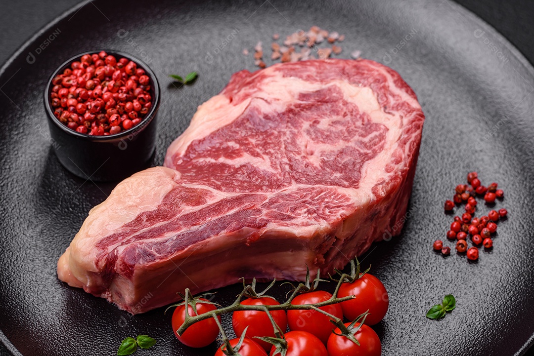 Bife fresco e suculento de carne crua com sal e especiarias sobre um fundo escuro de concreto