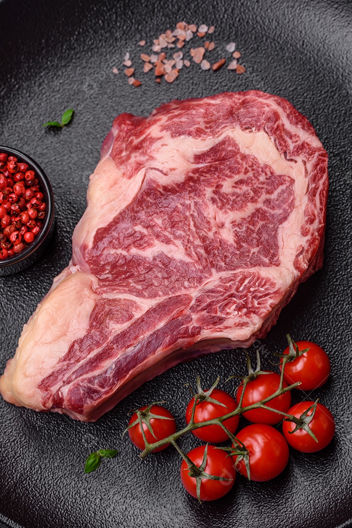 Bife fresco e suculento de carne crua com sal e especiarias sobre um fundo escuro de concreto