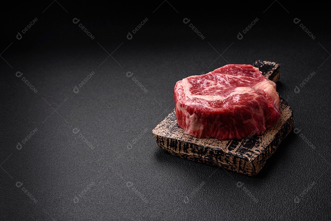 Bife fresco e suculento de carne crua com sal e especiarias sobre um fundo escuro de concreto