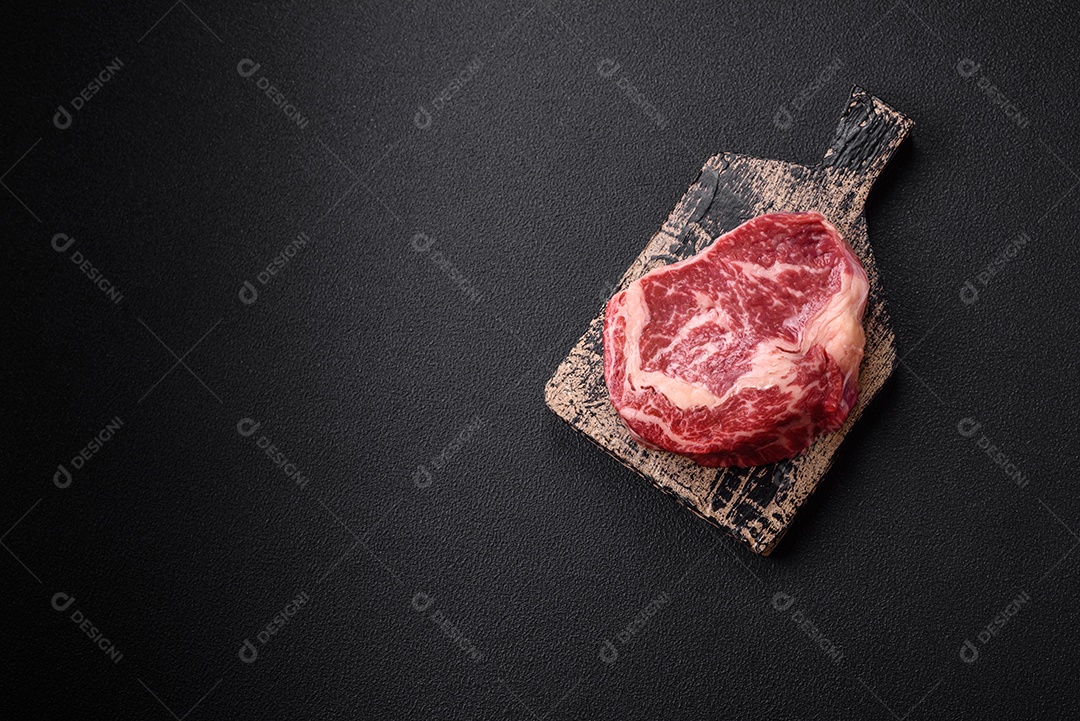 Bife fresco e suculento de carne crua com sal e especiarias sobre um fundo escuro de concreto