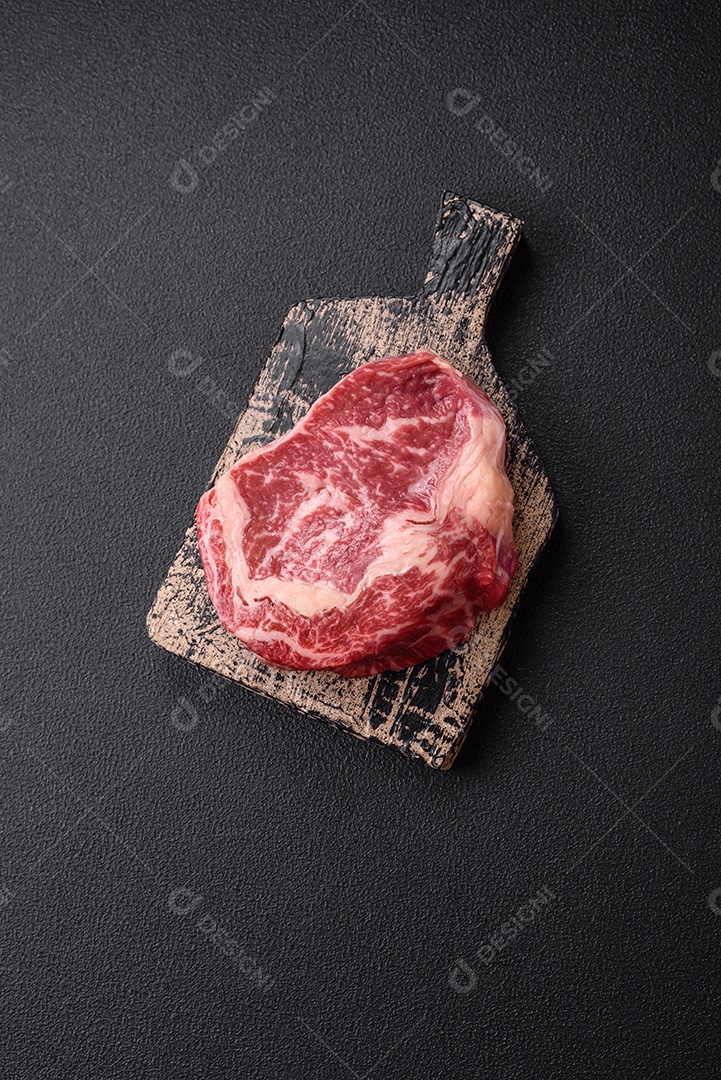 Bife fresco e suculento de carne crua com sal e especiarias sobre um fundo escuro de concreto