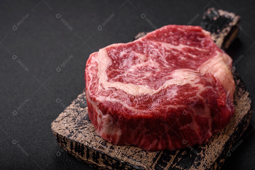 Bife fresco e suculento de carne crua com sal e especiarias sobre um fundo escuro de concreto