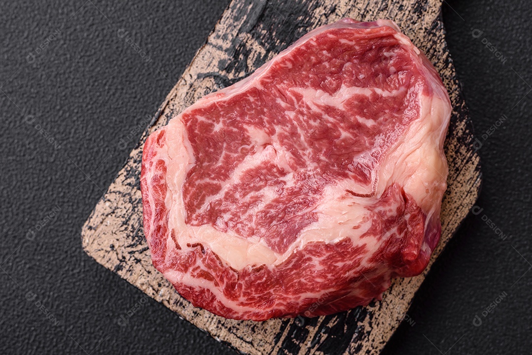 Bife fresco e suculento de carne crua com sal e especiarias sobre um fundo escuro de concreto