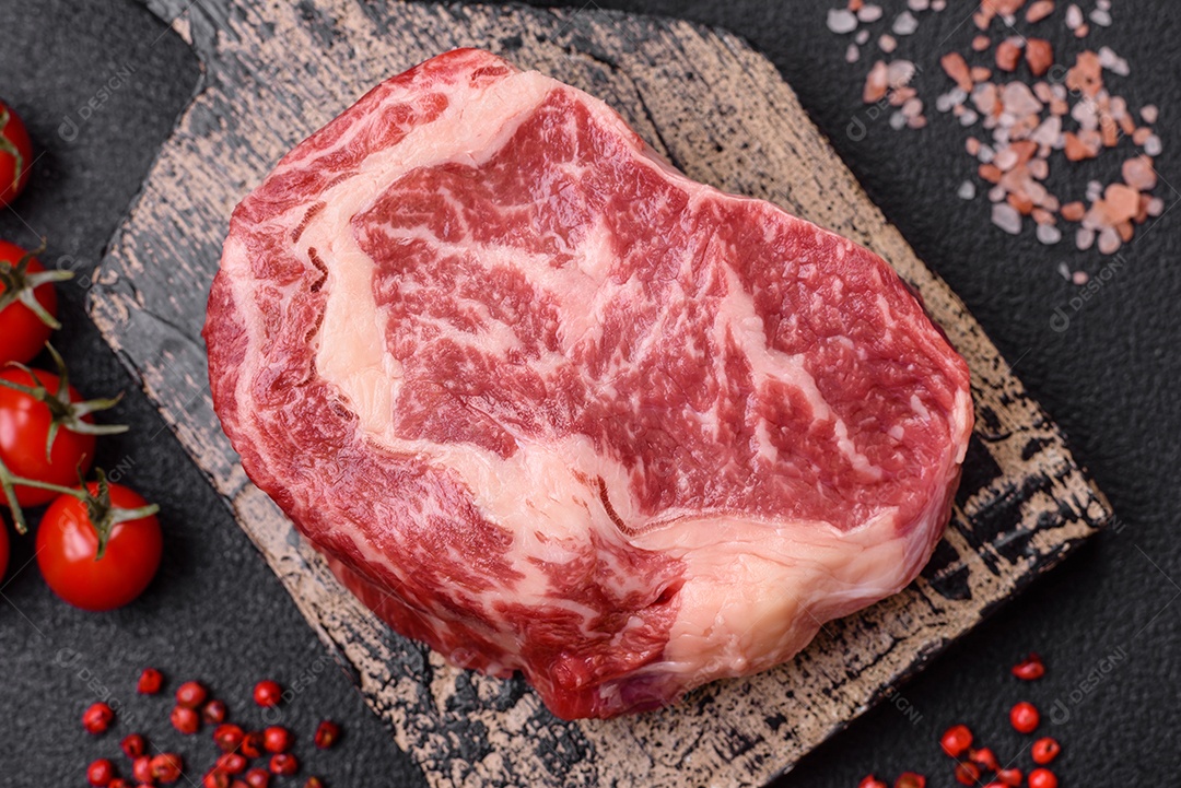 Bife fresco e suculento de carne crua com sal e especiarias sobre um fundo escuro de concreto