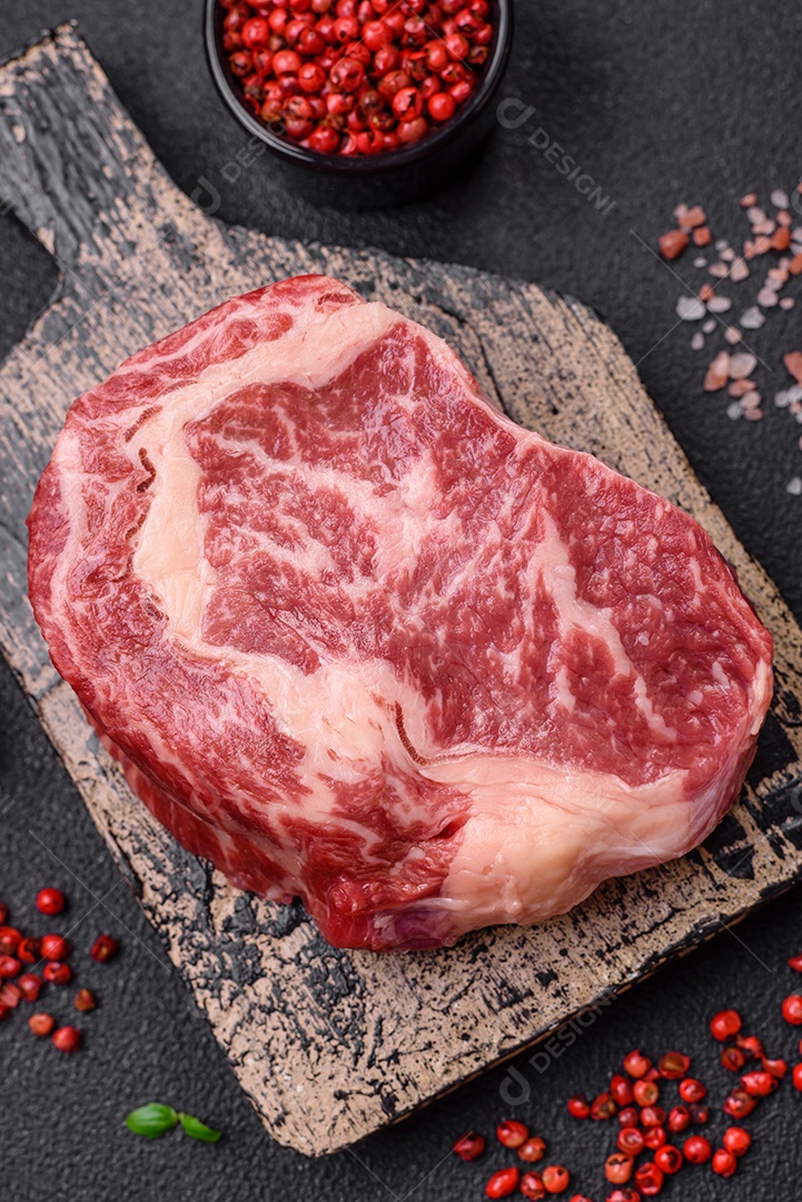Bife fresco e suculento de carne crua com sal e especiarias sobre um fundo escuro de concreto