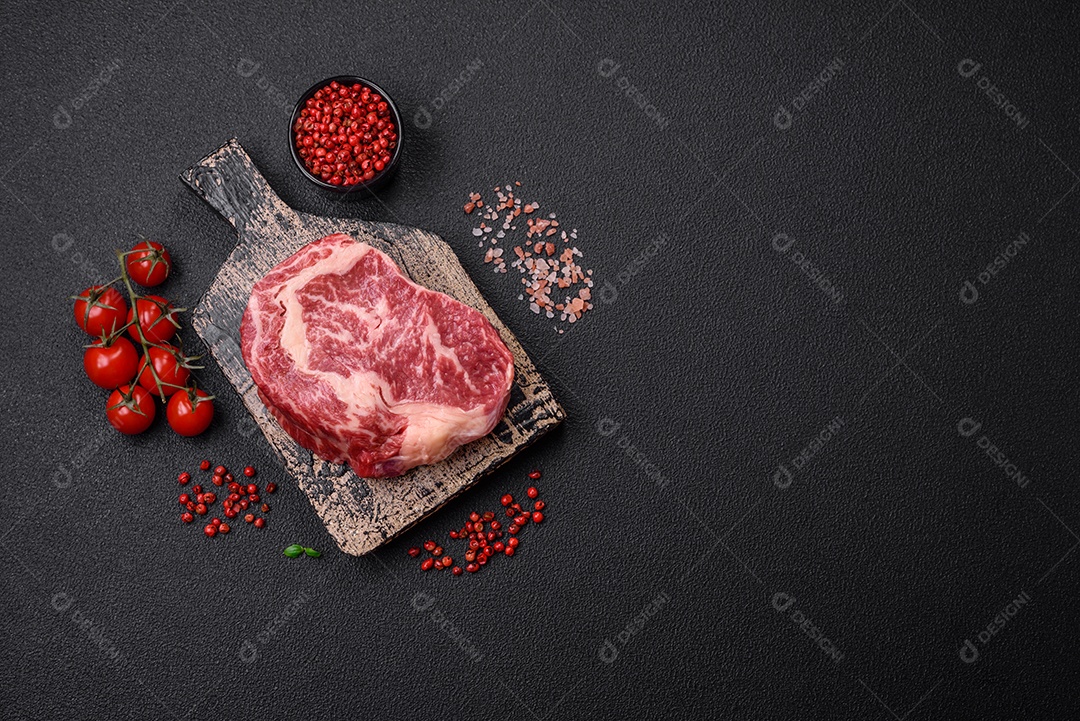 Bife fresco e suculento de carne crua com sal e especiarias sobre um fundo escuro de concreto