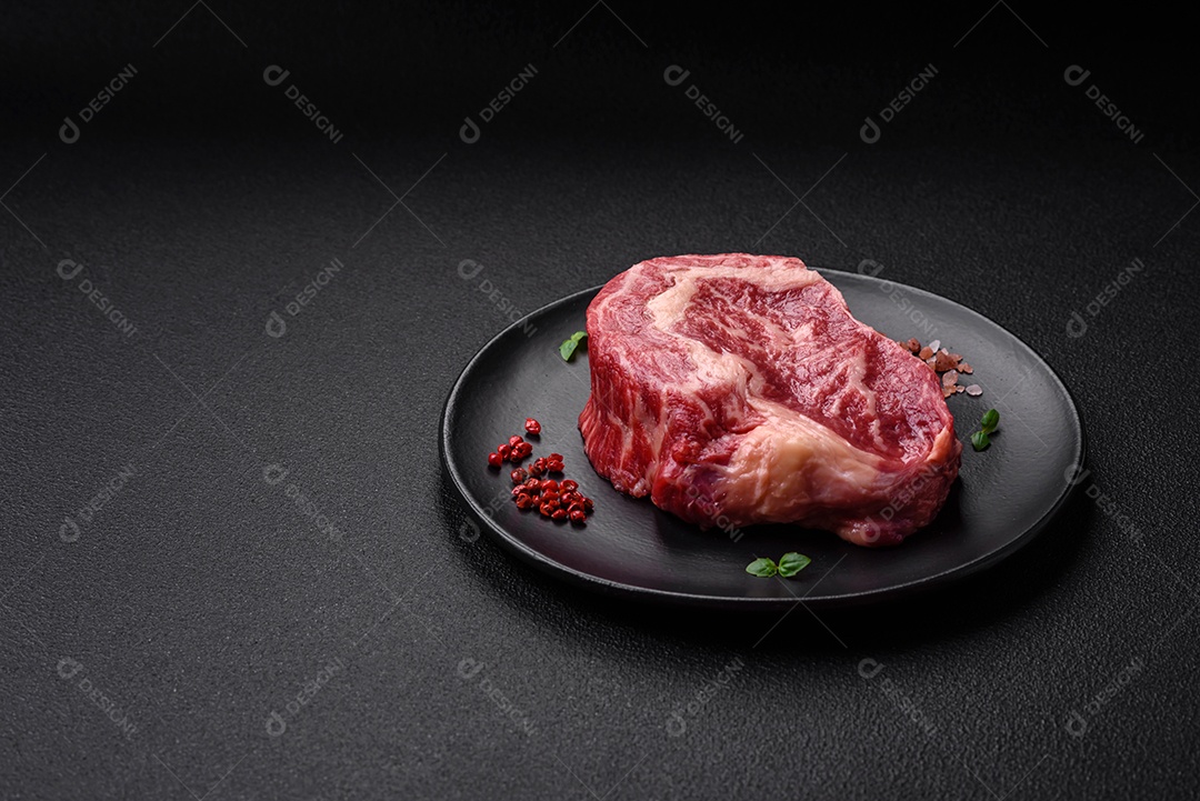Bife fresco e suculento de carne crua com sal e especiarias sobre um fundo escuro de concreto
