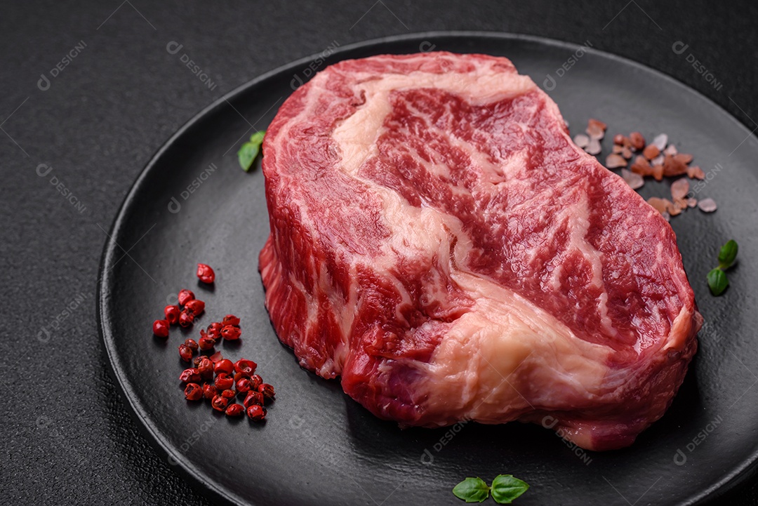 Bife fresco e suculento de carne crua com sal e especiarias sobre um fundo escuro de concreto