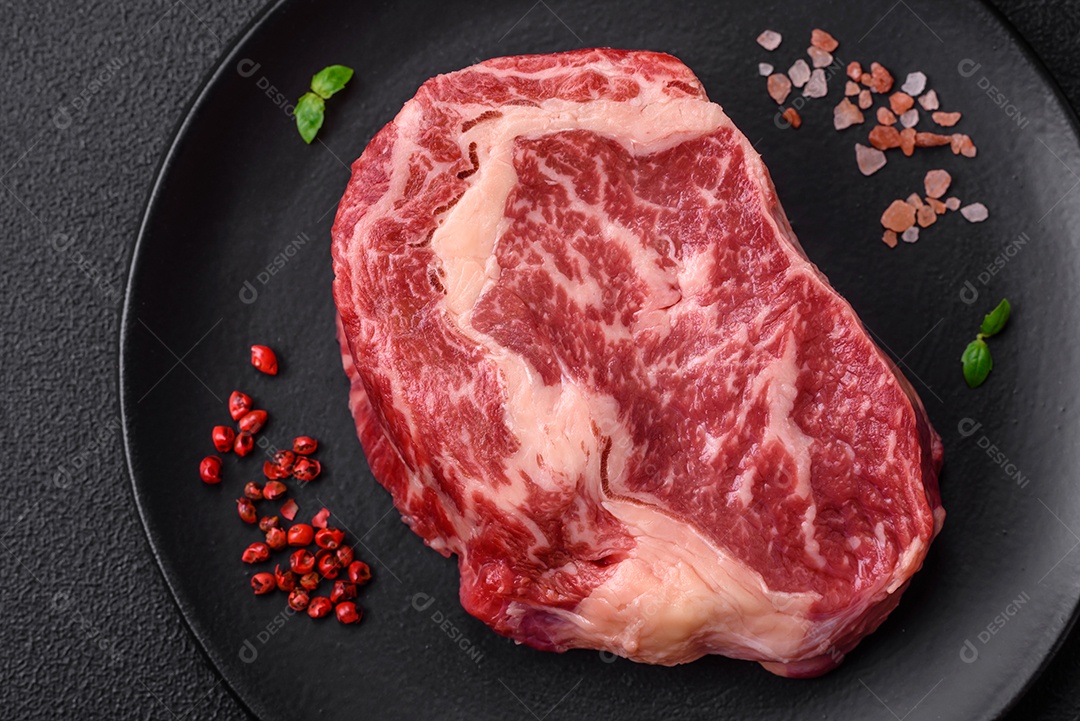 Bife fresco e suculento de carne crua com sal e especiarias sobre um fundo escuro de concreto