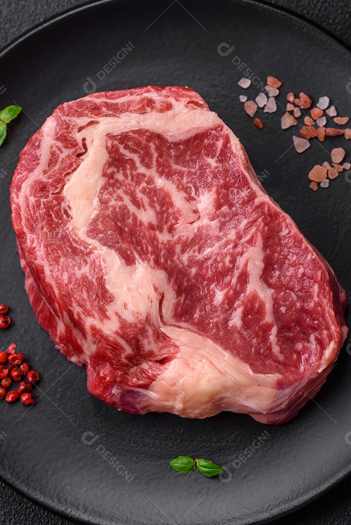 Bife fresco e suculento de carne crua com sal e especiarias sobre um fundo escuro de concreto