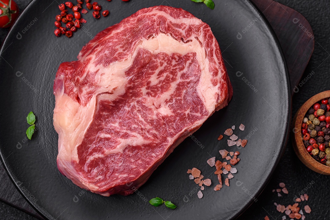 Bife fresco e suculento de carne crua com sal e especiarias sobre um fundo escuro de concreto
