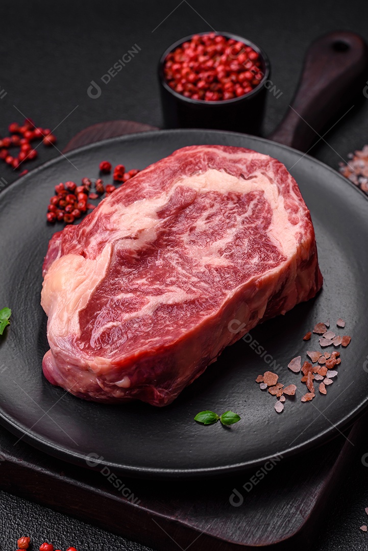 Bife fresco e suculento de carne crua com sal e especiarias sobre um fundo escuro de concreto