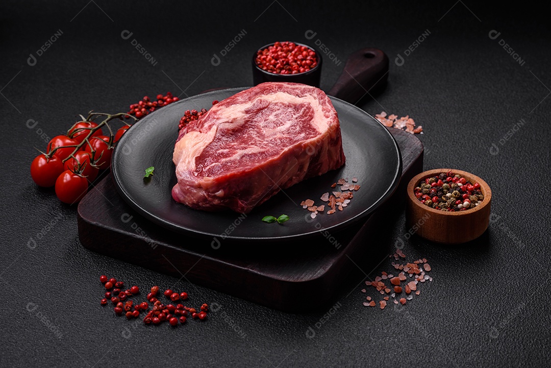 Bife fresco e suculento de carne crua com sal e especiarias sobre um fundo escuro de concreto
