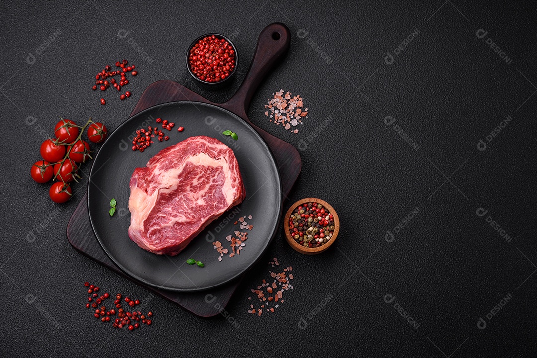 Bife fresco e suculento de carne crua com sal e especiarias sobre um fundo escuro de concreto