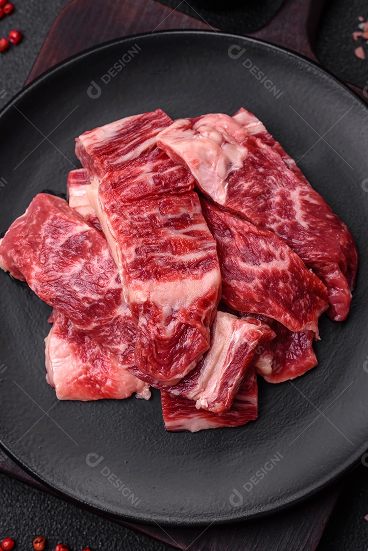 Bife fresco e suculento de carne crua com sal e especiarias sobre um fundo escuro de concreto