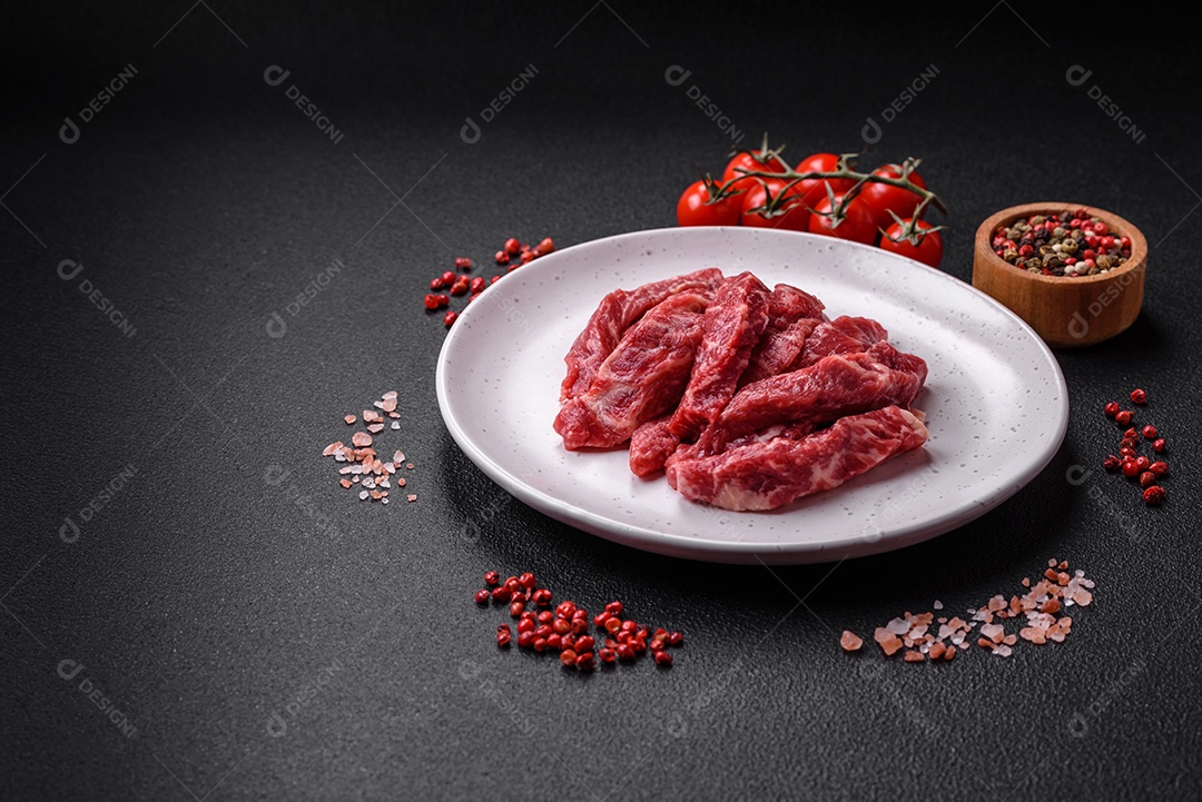 Fatias frescas e suculentas de carne crua com sal e especiarias sobre um fundo escuro de concreto