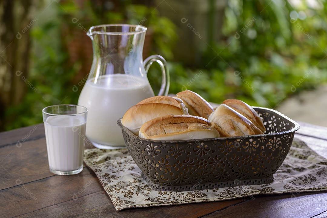 Pão em uma cesta e leite em uma jarra de vidro sobre uma mesa de madeira