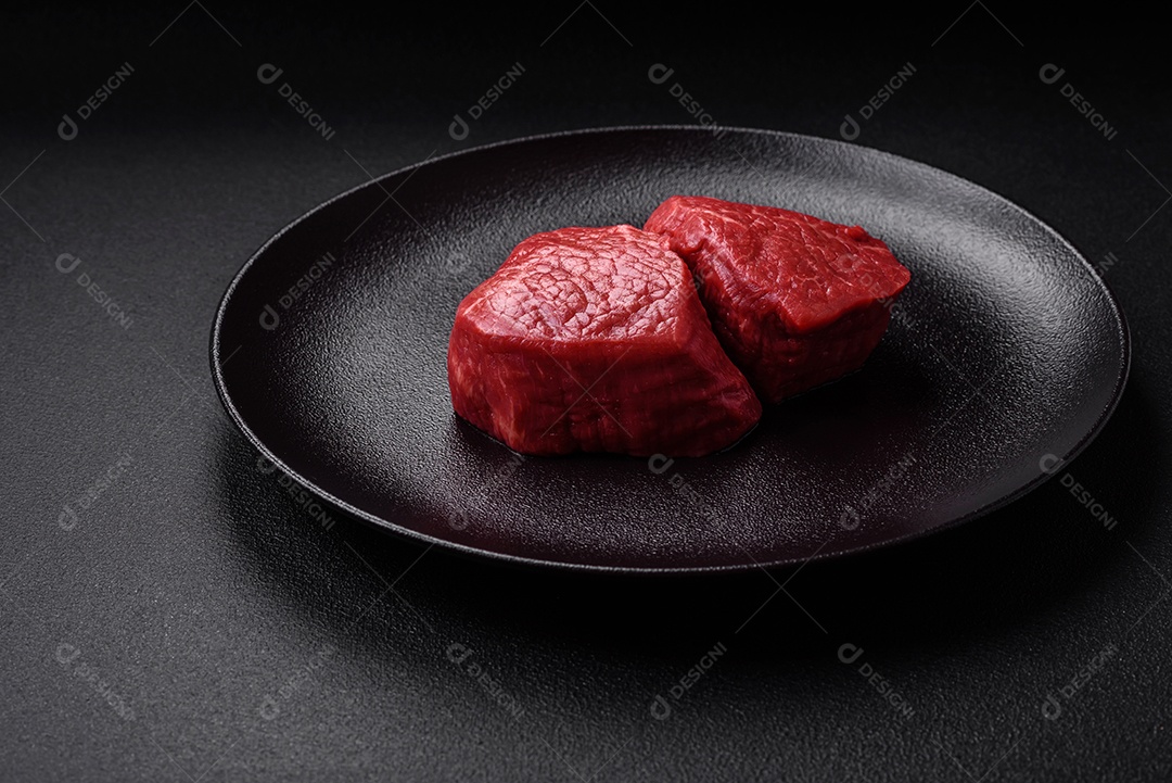 Medalhões frescos e suculentos de carne crua com sal e especiarias sobre um fundo escuro de concreto