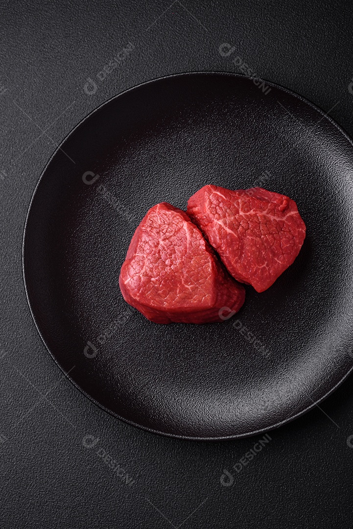 Medalhões frescos e suculentos de carne crua com sal e especiarias sobre um fundo escuro de concreto