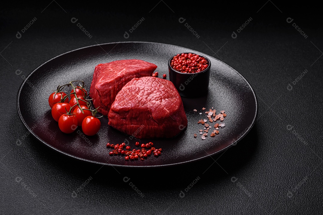 Medalhões frescos e suculentos de carne crua com sal e especiarias sobre um fundo escuro de concreto