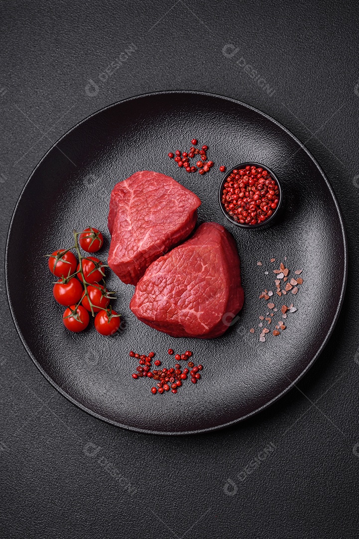 Medalhões frescos e suculentos de carne crua com sal e especiarias sobre um fundo escuro de concreto