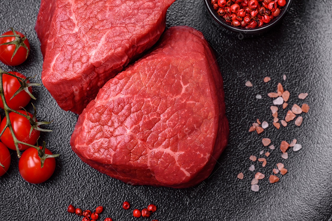 Medalhões frescos e suculentos de carne crua com sal e especiarias sobre um fundo escuro de concreto