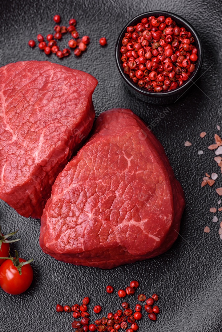 Medalhões frescos e suculentos de carne crua com sal e especiarias sobre um fundo escuro de concreto