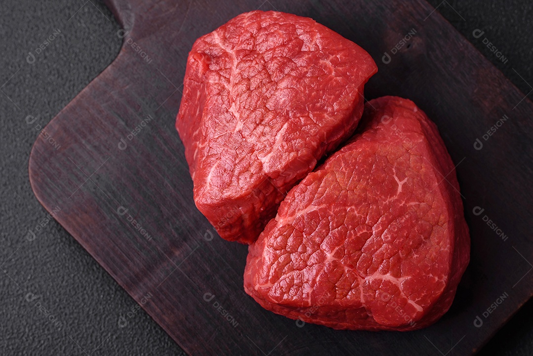 Medalhões frescos e suculentos de carne crua com sal e especiarias sobre um fundo escuro de concreto