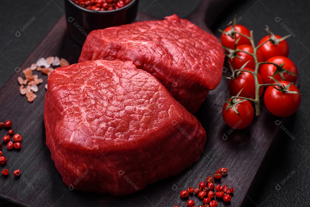 Medalhões frescos e suculentos de carne crua com sal e especiarias sobre um fundo escuro de concreto