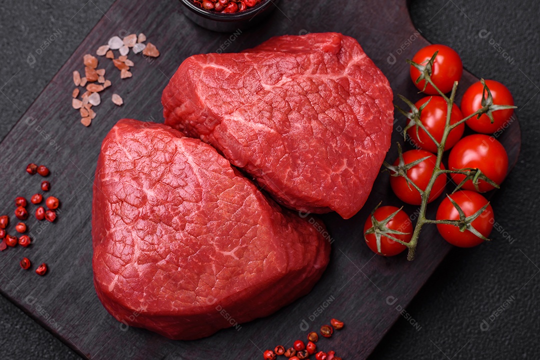 Medalhões frescos e suculentos de carne crua com sal e especiarias sobre um fundo escuro de concreto