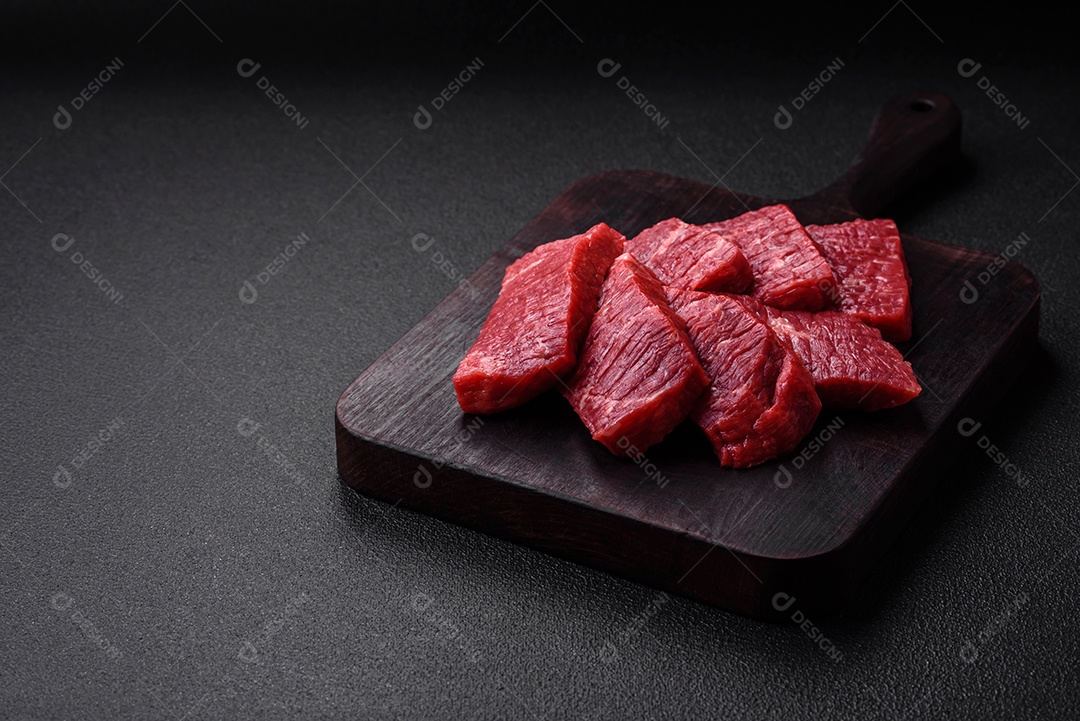 Fatias frescas e suculentas de carne crua com sal e especiarias sobre um fundo escuro de concreto