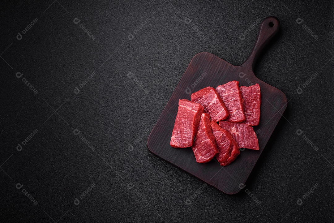 Fatias frescas e suculentas de carne crua com sal e especiarias sobre um fundo escuro de concreto