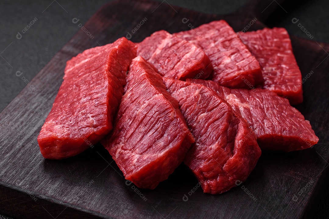 Fatias frescas e suculentas de carne crua com sal e especiarias sobre um fundo escuro de concreto