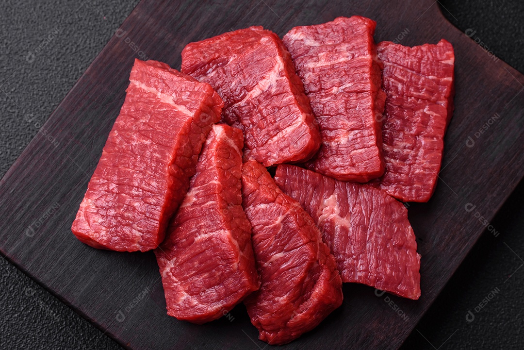 Fatias frescas e suculentas de carne crua com sal e especiarias sobre um fundo escuro de concreto