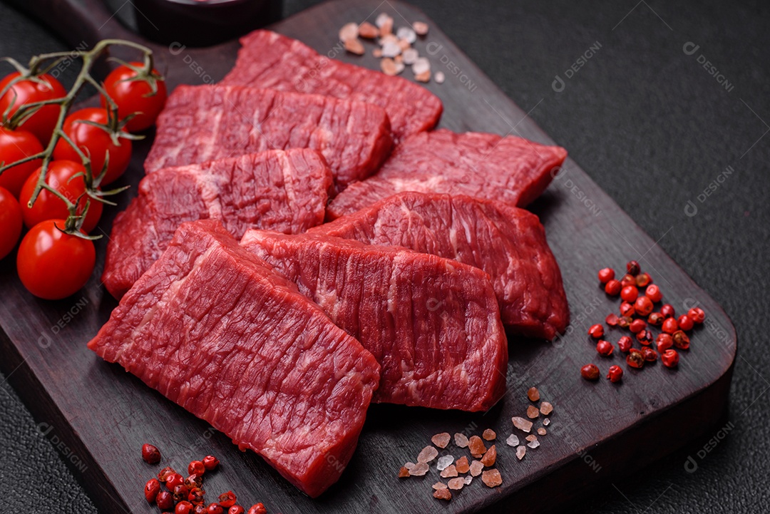 Fatias frescas e suculentas de carne crua com sal e especiarias sobre um fundo escuro de concreto