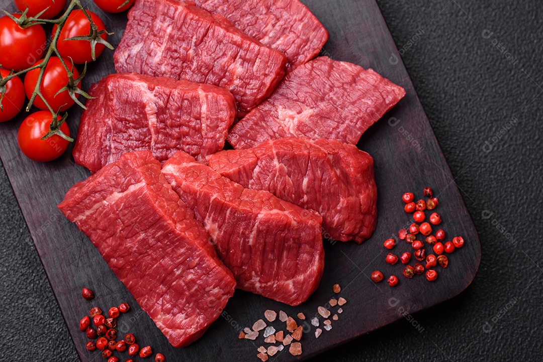 Fatias frescas e suculentas de carne crua com sal e especiarias sobre um fundo escuro de concreto