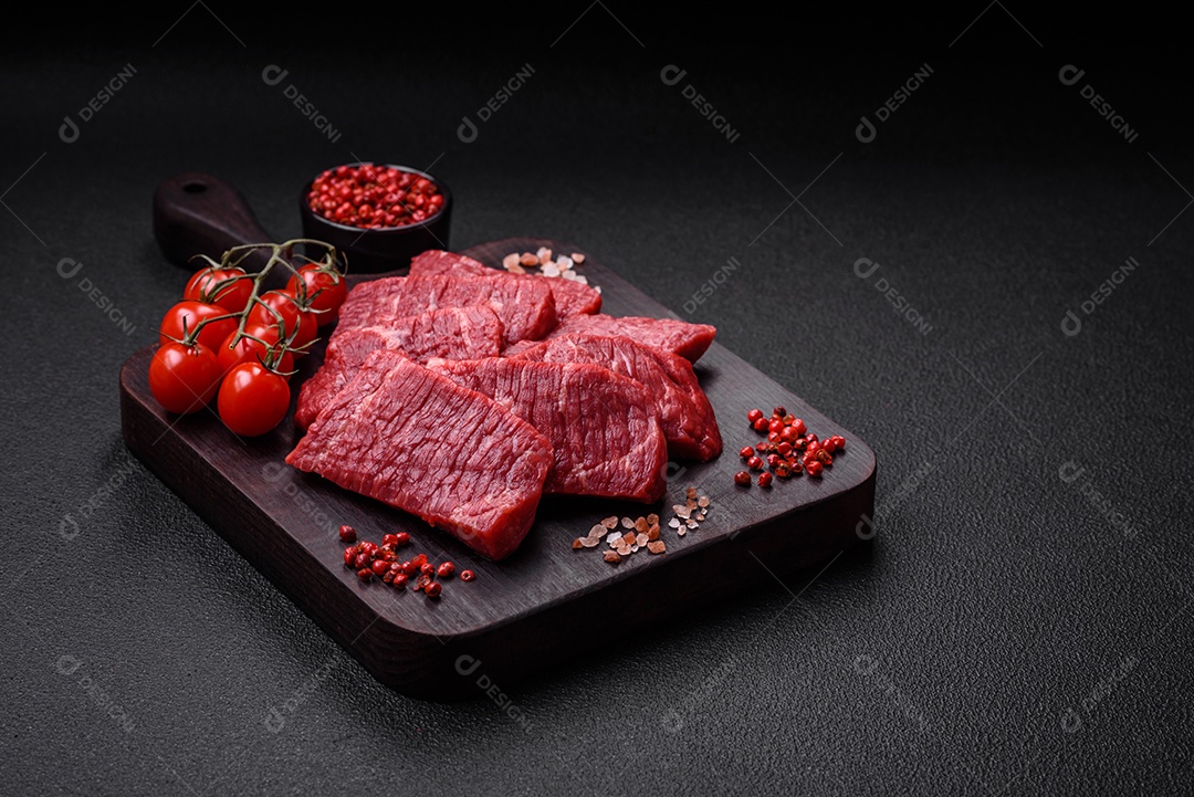 Fatias frescas e suculentas de carne crua com sal e especiarias sobre um fundo escuro de concreto
