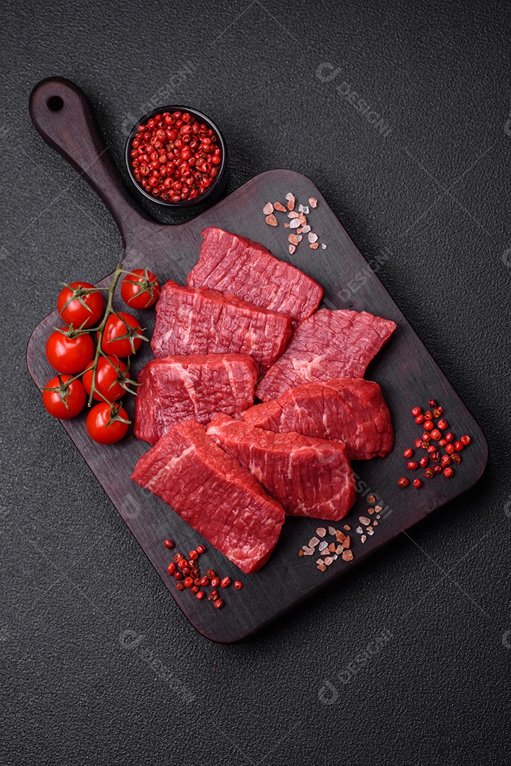Fatias frescas e suculentas de carne crua com sal e especiarias sobre um fundo escuro de concreto
