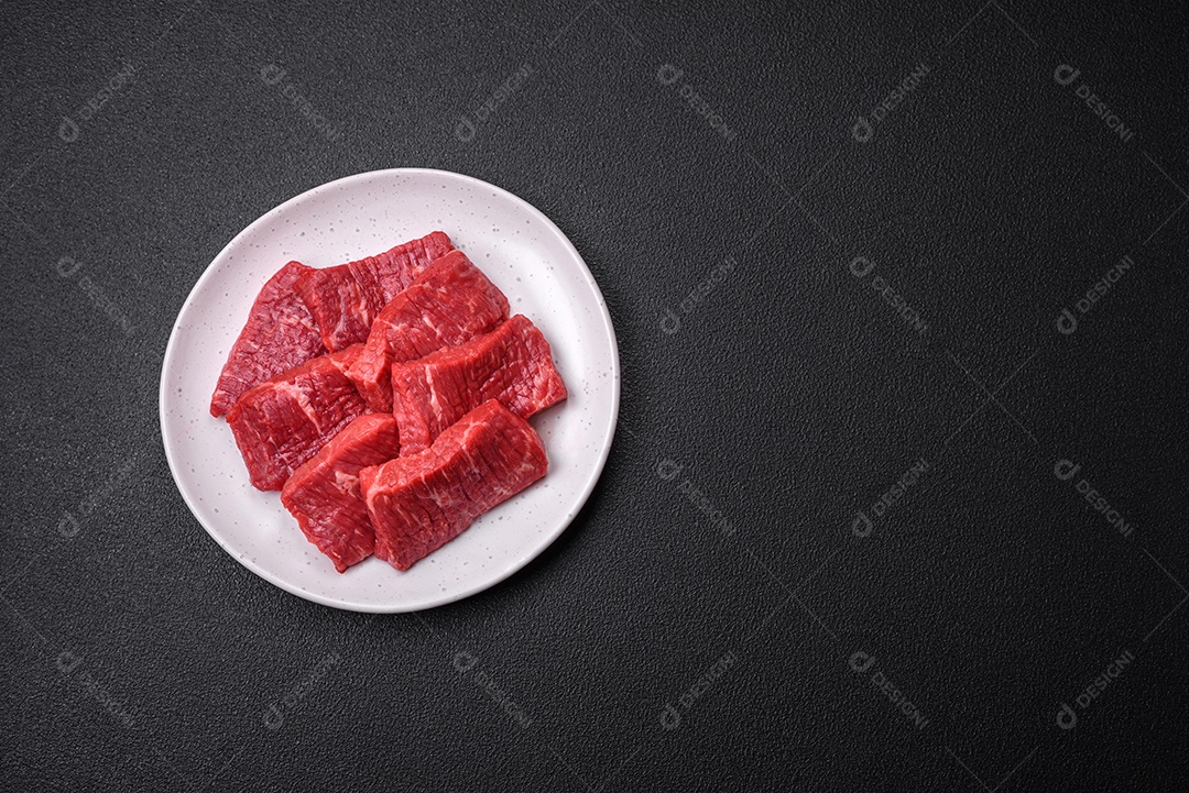 Fatias frescas e suculentas de carne crua com sal e especiarias sobre um fundo escuro de concreto