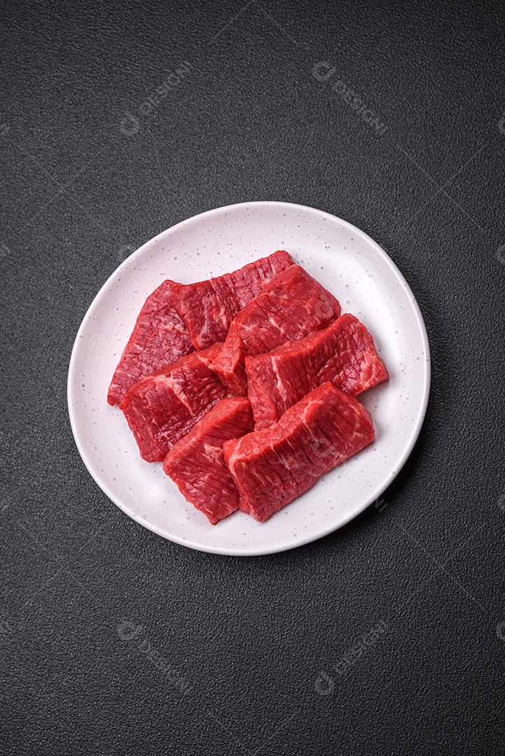 Fatias frescas e suculentas de carne crua com sal e especiarias sobre um fundo escuro de concreto