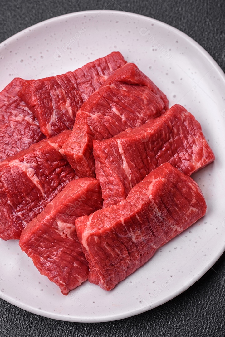 Fatias frescas e suculentas de carne crua com sal e especiarias sobre um fundo escuro de concreto