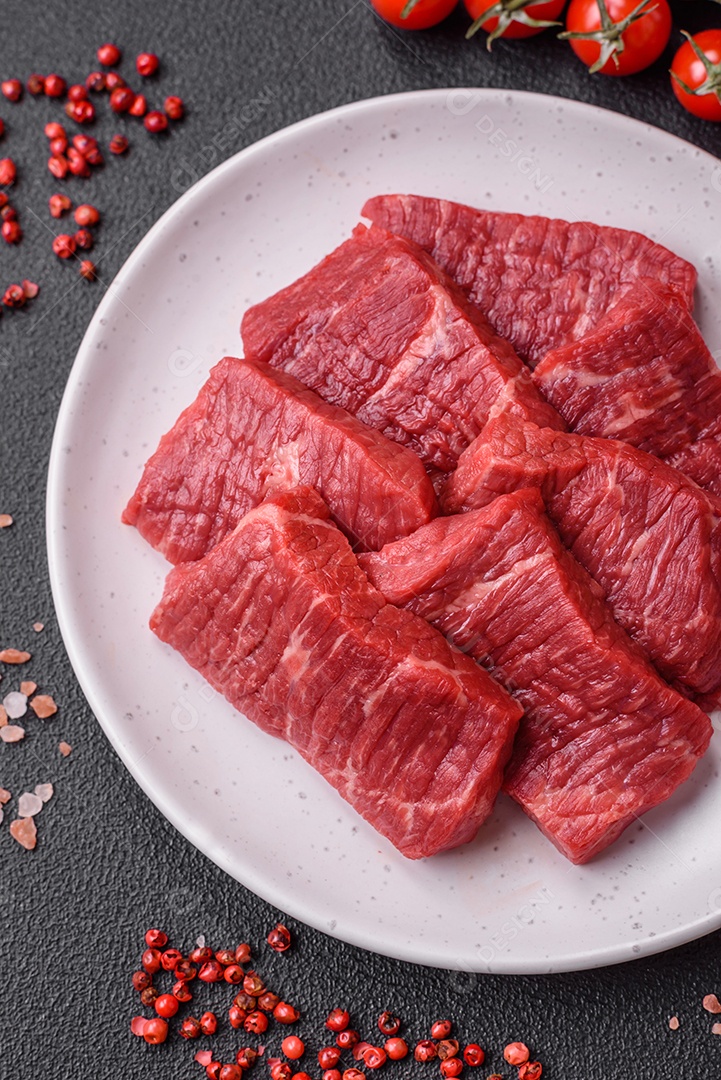 Fatias frescas e suculentas de carne crua com sal e especiarias sobre um fundo escuro de concreto