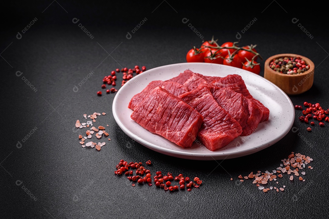 Fatias frescas e suculentas de carne crua com sal e especiarias sobre um fundo escuro de concreto