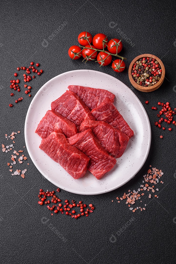 Fatias frescas e suculentas de carne crua com sal e especiarias sobre um fundo escuro de concreto